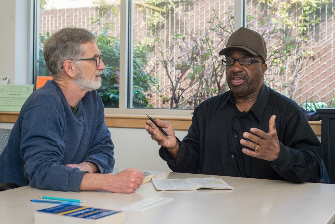 Two men, seated at a table, talking